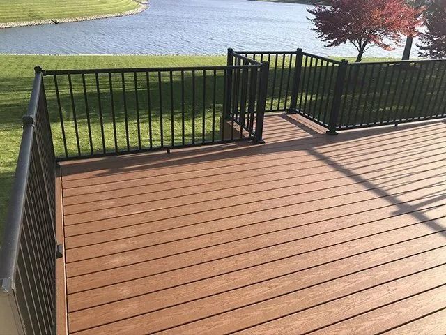 Brown deck with black railing overlooking water and green grass.