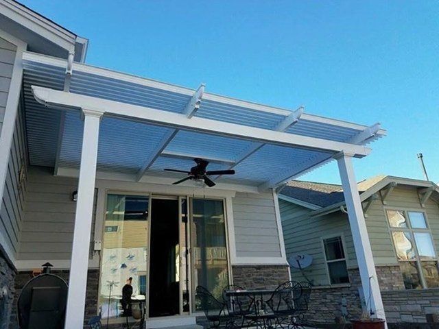 White patio cover attached to a house with a ceiling fan. Sunny blue sky.