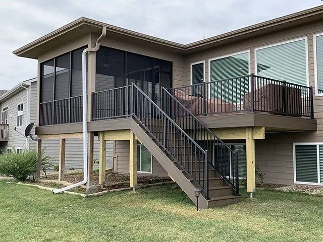 Back of a house with a deck and screened-in porch. The deck has dark brown railings and stairs.