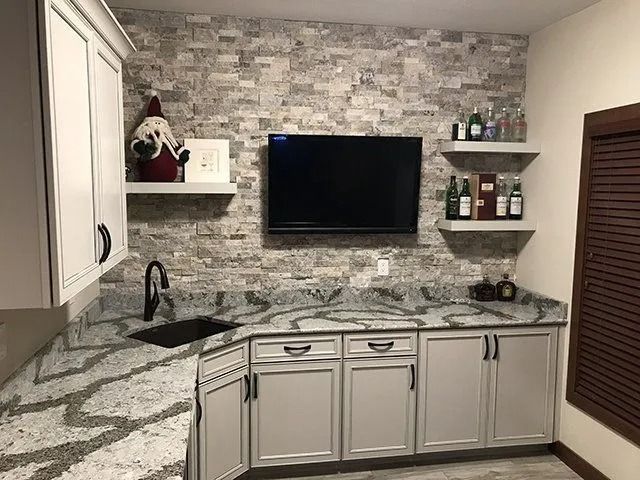 Wet bar with stone accent wall, granite countertop, cabinets, and a mounted TV.