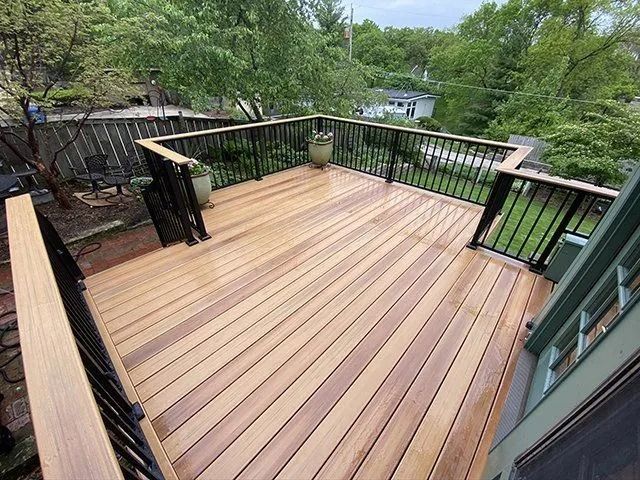 Wooden deck with black railings and potted plants, surrounded by greenery.