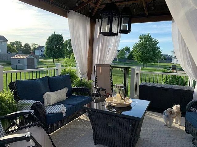 Outdoor patio with blue furniture, white curtains, and a gazebo overlooking a yard. A dog stands nearby.