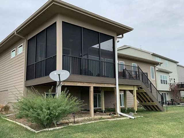 Beige house with a screened-in porch and deck, black railings, satellite dish, and stairs leading down.