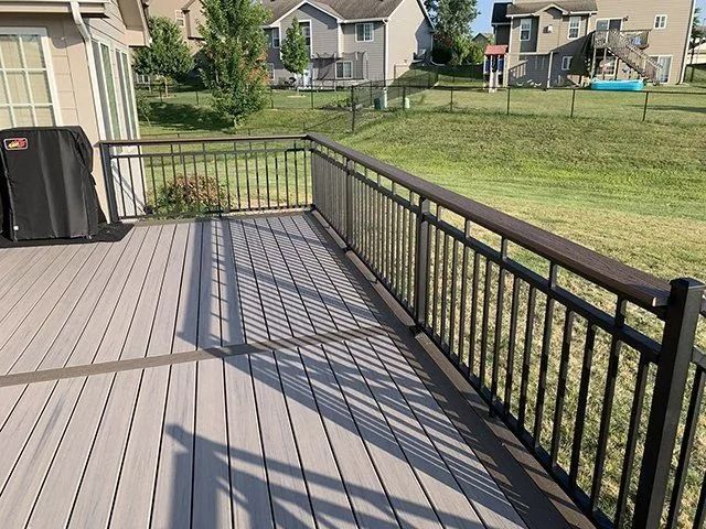 Deck with gray composite boards, black railing, and a dark brown top rail. Back yard setting.