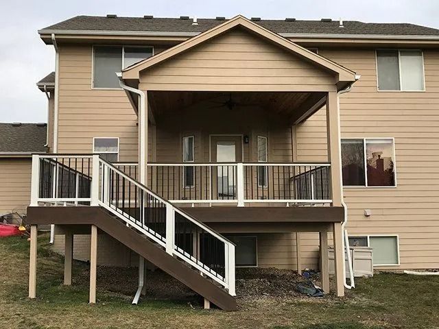 Beige house with a covered deck, brown stairs, and black and white railings.