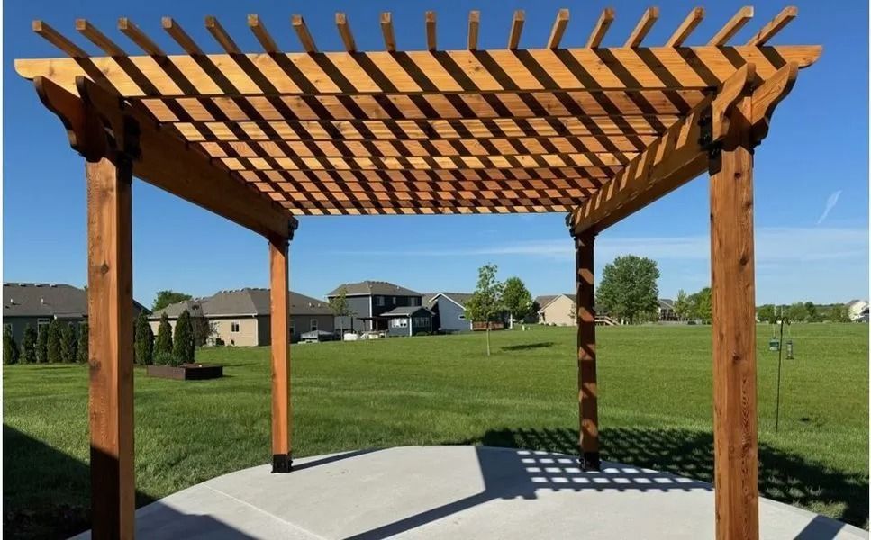 Wooden pergola with slatted roof over a concrete patio, grassy yard, and blue sky.