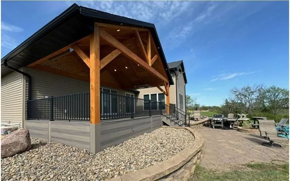 Deck with wooden pergola, black railing, composite decking, and rock border, against a blue sky.