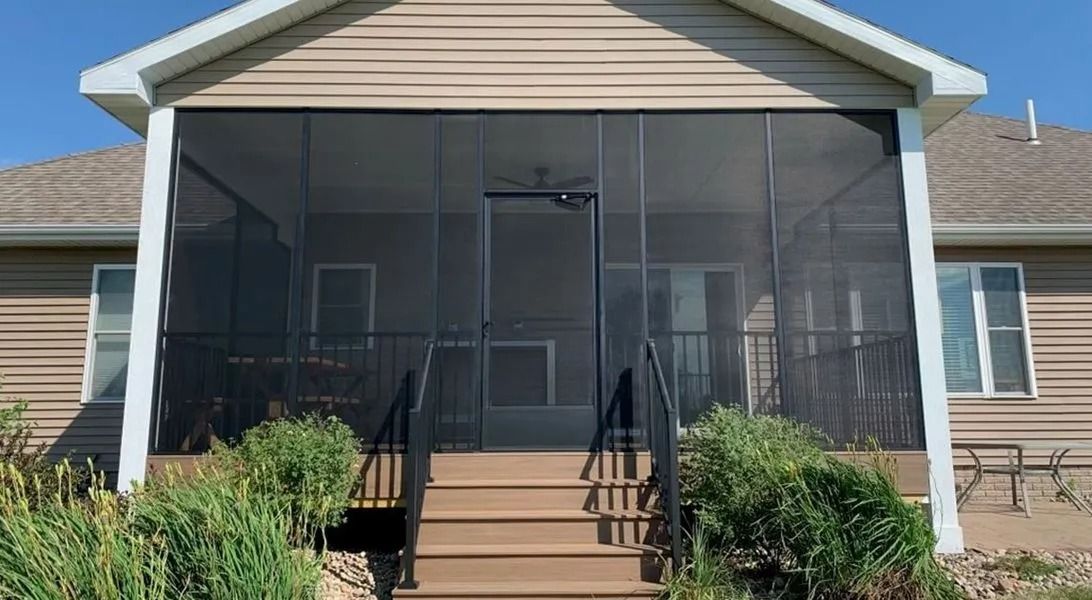Screened-in porch with steps, a black door, and a tan house with windows. Green bushes in foreground.