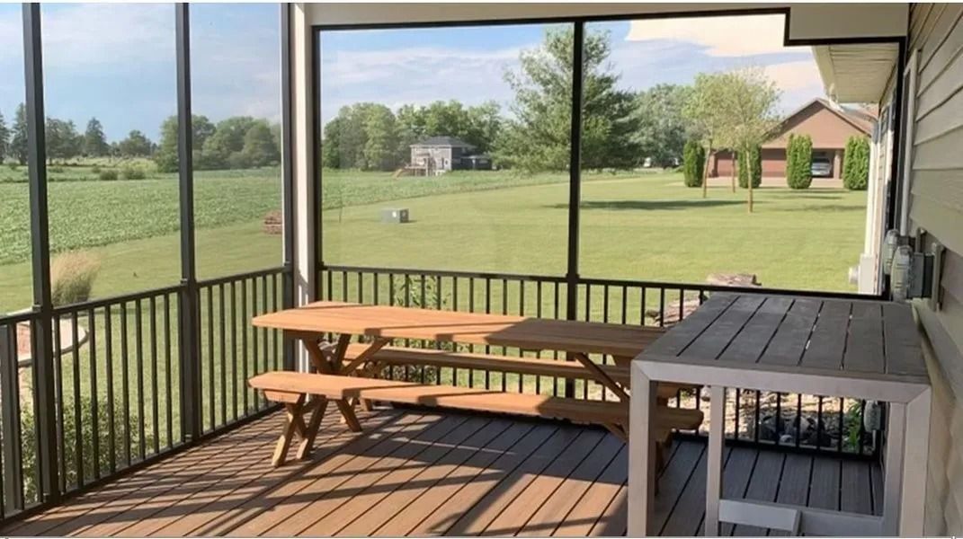 Screened porch with picnic table, outdoor view of field and distant buildings.