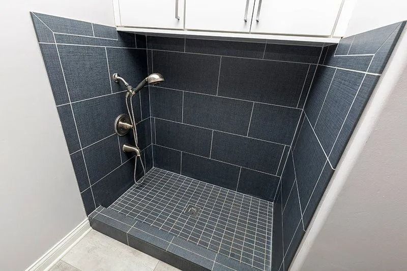Dark tile shower with silver showerhead and fixtures. White grout. Recessed design.