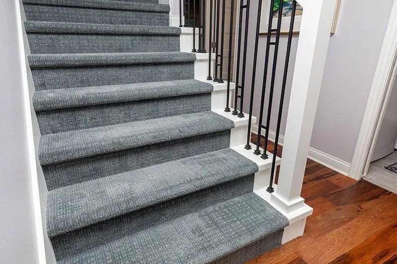 Gray carpeted staircase with black railing and hardwood floor landing.