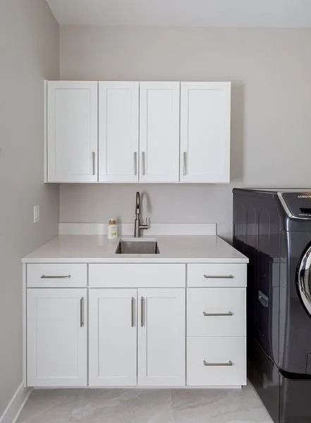 White laundry room with sink, cabinets, and a dark washing machine.