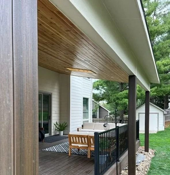 Covered porch with wood ceiling and seating area, overlooking a backyard with a shed.