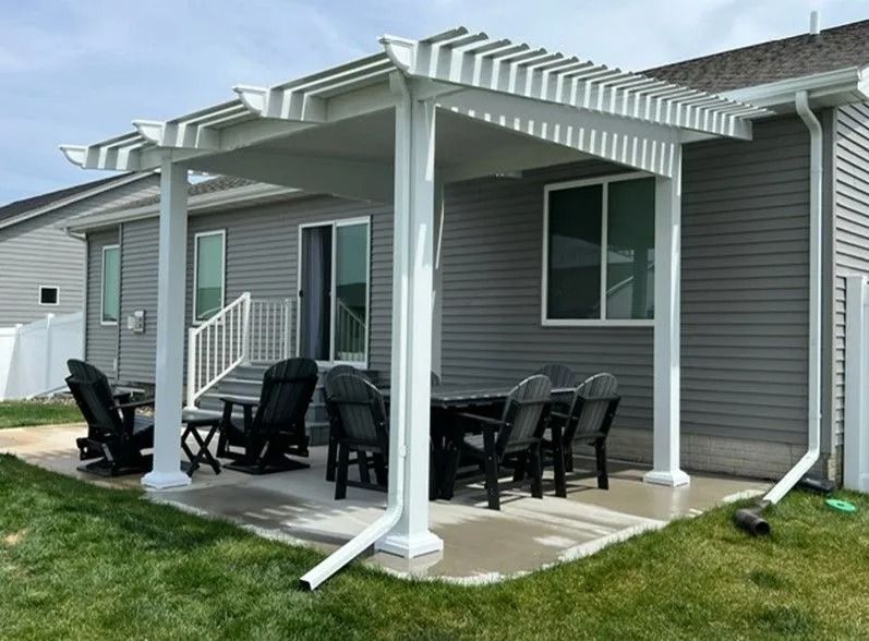 Pergola over patio with a dining table and chairs near a house with gray siding.