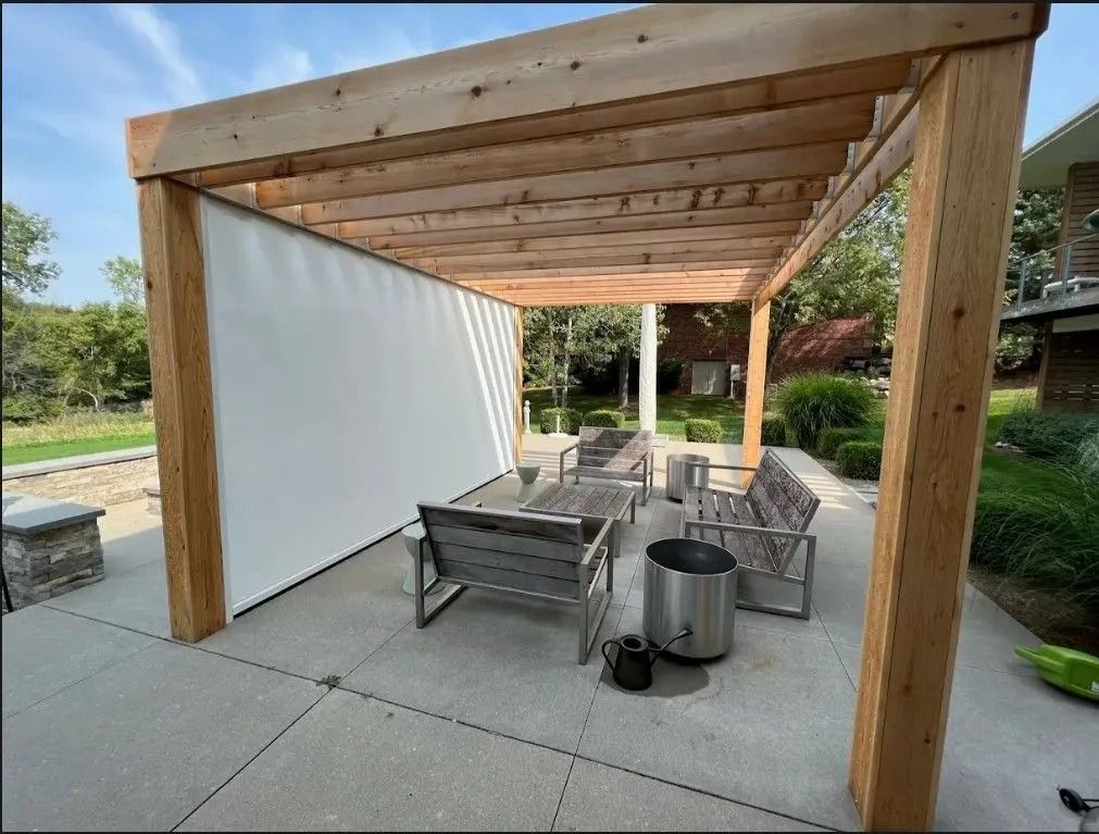Wooden pergola over a patio with white shade screen and outdoor furniture.