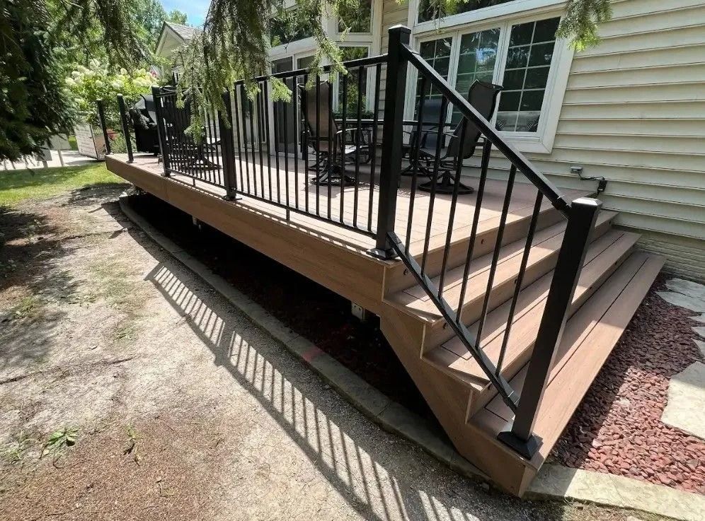 Brown composite deck with black railing and stairs next to a beige house, yard in foreground.