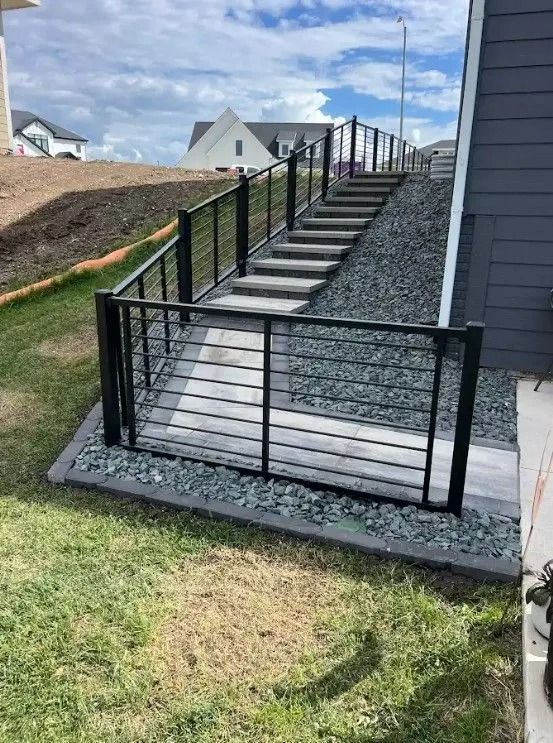 Outdoor staircase with black metal railings, leading up a hillside.