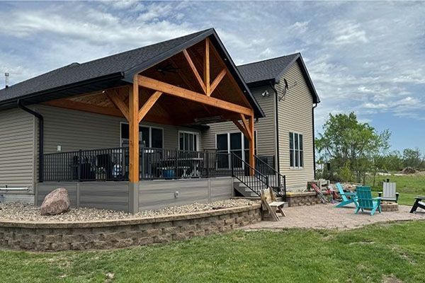 A house with a wooden patio cover, deck, and brick patio. Landscaped yard with outdoor seating.