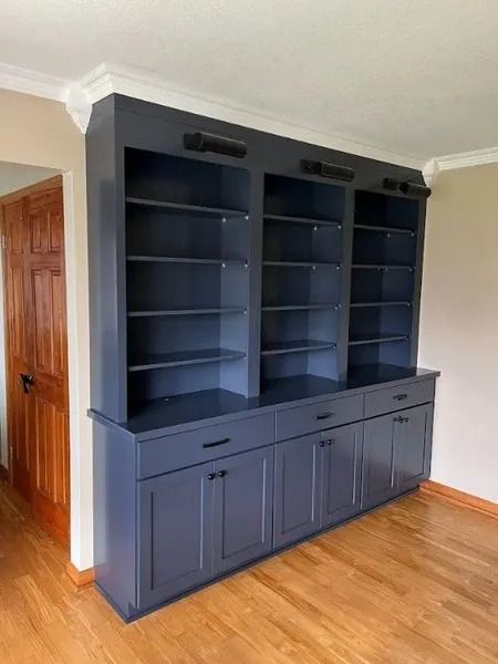 Built-in blue bookcase with shelves, drawers, and cabinets, against a white wall and wood floor.