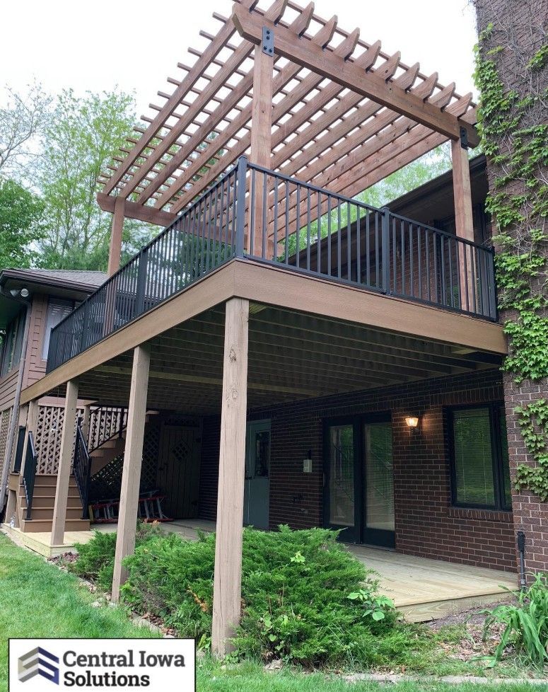 Two-story deck with pergola; brown wood and black railings. Building has brick and siding.