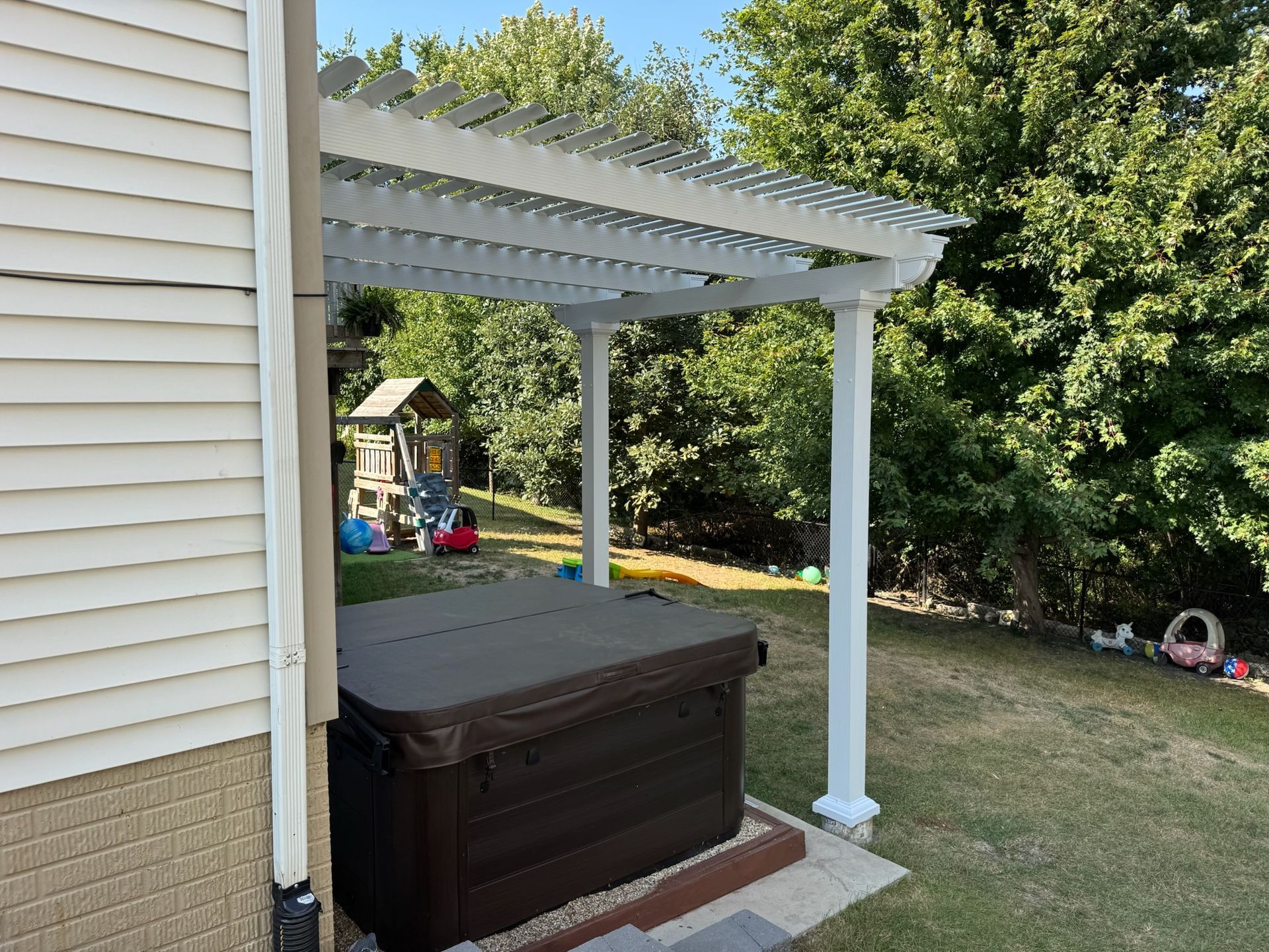 Backyard patio with a white pergola, brown hot tub, and grassy yard beside a house