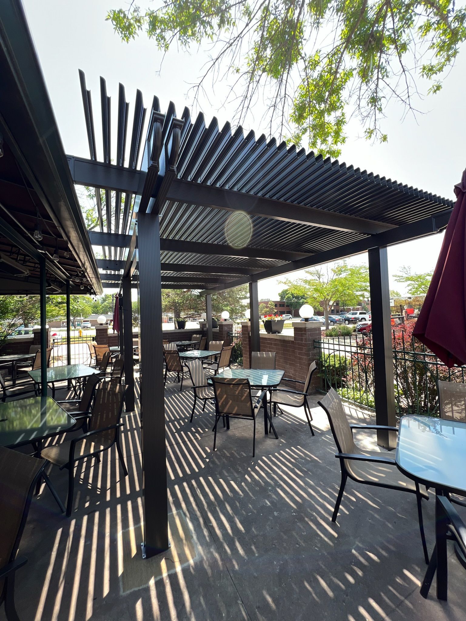 Outdoor café patio with black pergola, striped shadows, and empty tables and chairs