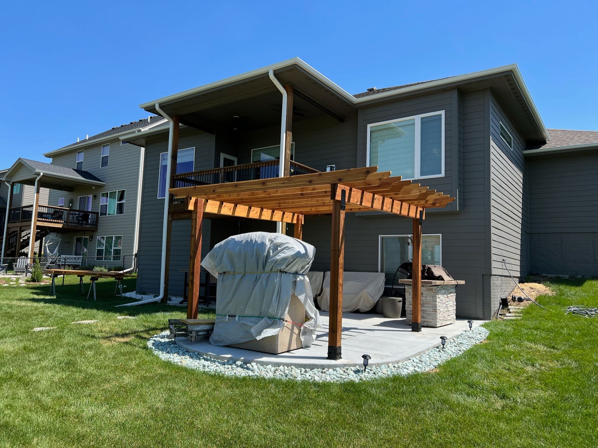 Backyard patio with wooden pergola, covered grill, and outdoor seating beside a house