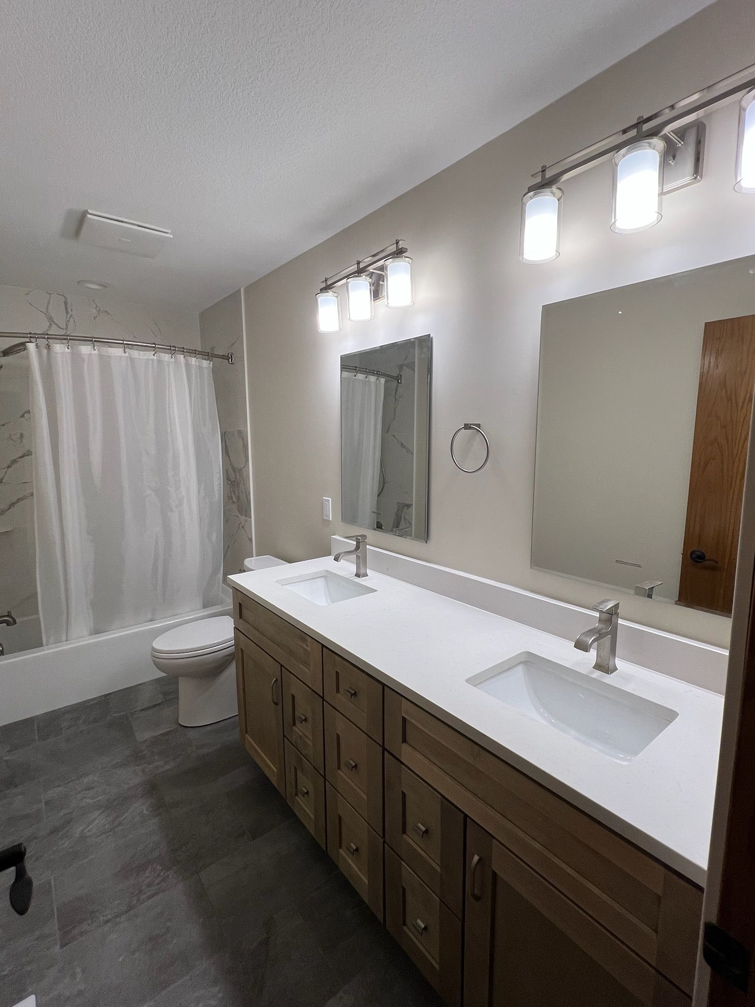 Modern bathroom with double vanity, large mirror, toilet, and shower curtain on gray tile floor