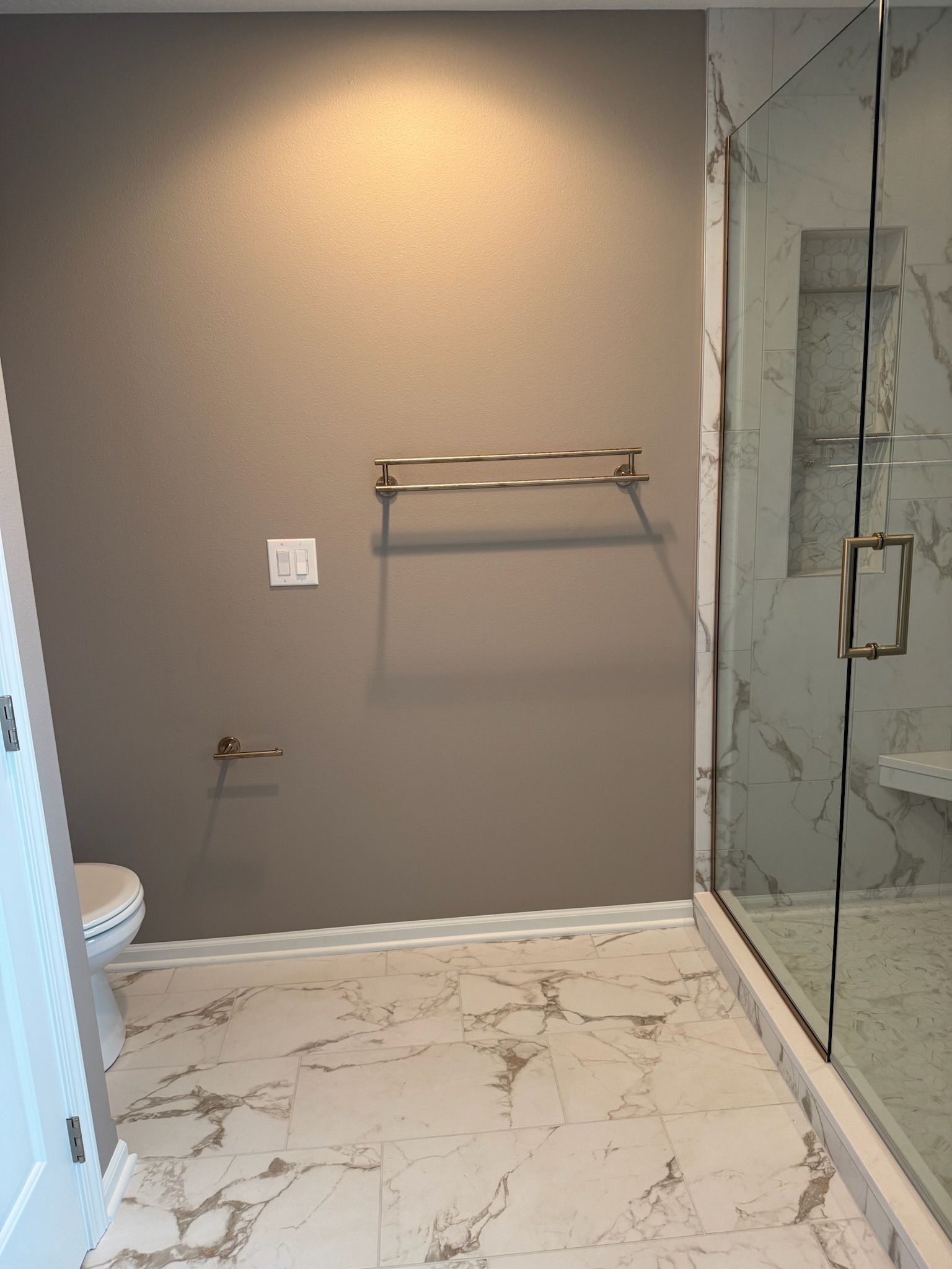 Modern bathroom with marble floor, glass shower, towel bar, and warm beige walls