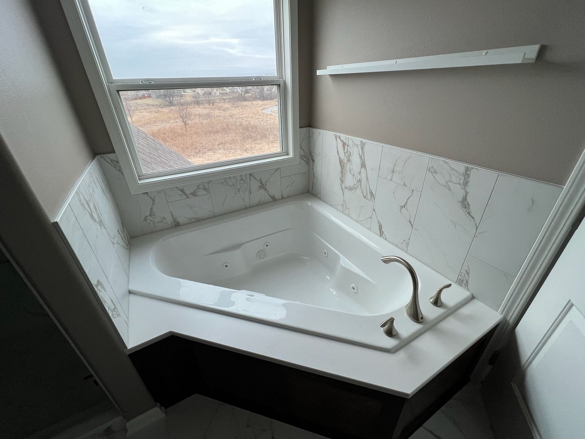 Corner bathtub with marble walls and a window overlooking a landscape.