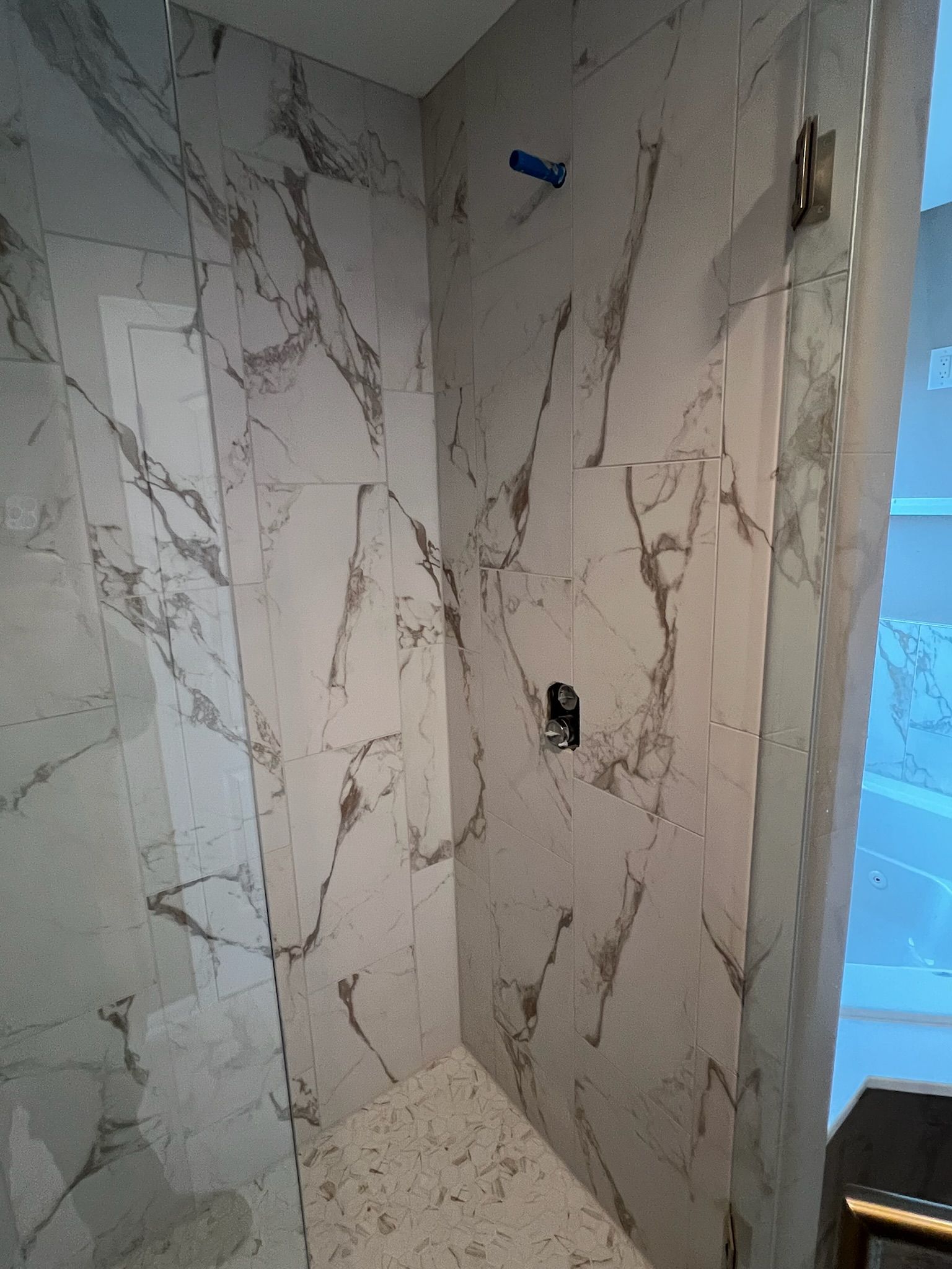 Tiled shower nook with marble-look walls, a small ledge, and a blue object mounted near the top.