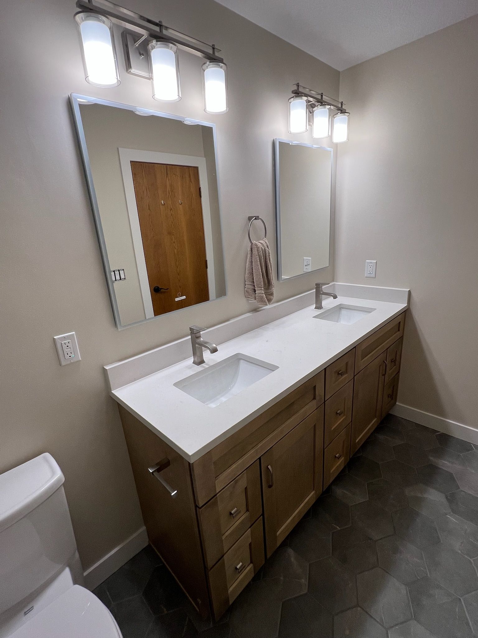 Bathroom vanity with double mirrors, white countertop, wood cabinets, and two light fixtures above.