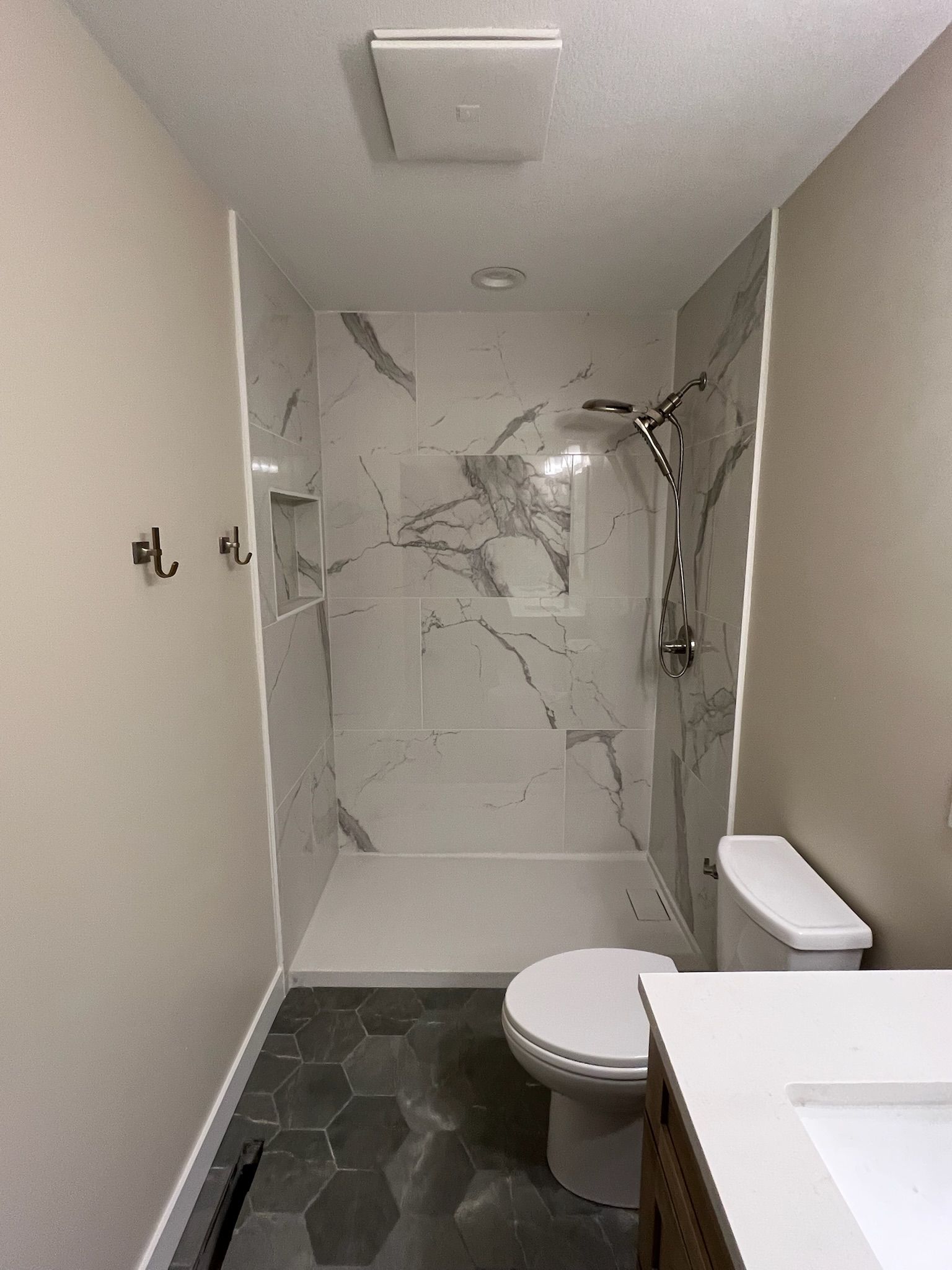 Narrow bathroom with white marble shower, toilet, and dark tile floor.