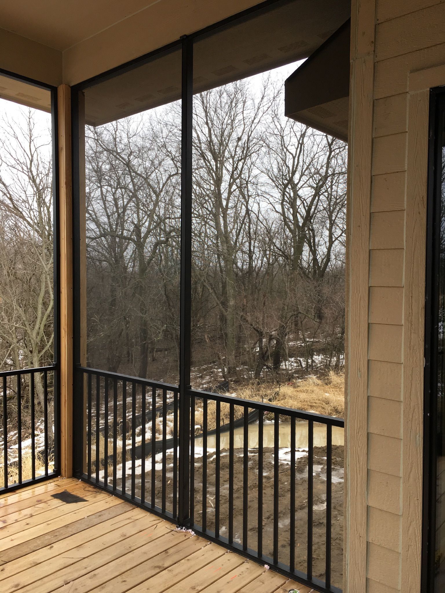 Covered porch with black railing overlooking leafless trees and a wintery yard