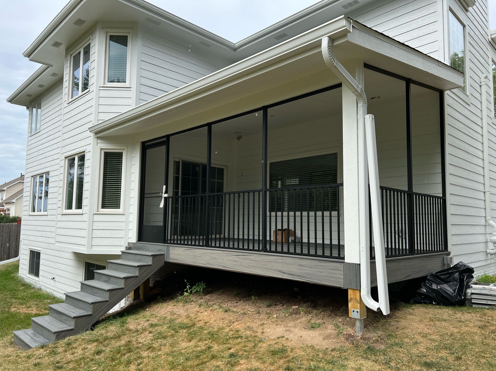 White house with covered porch, black railings, and steps leading to a grassy yard.