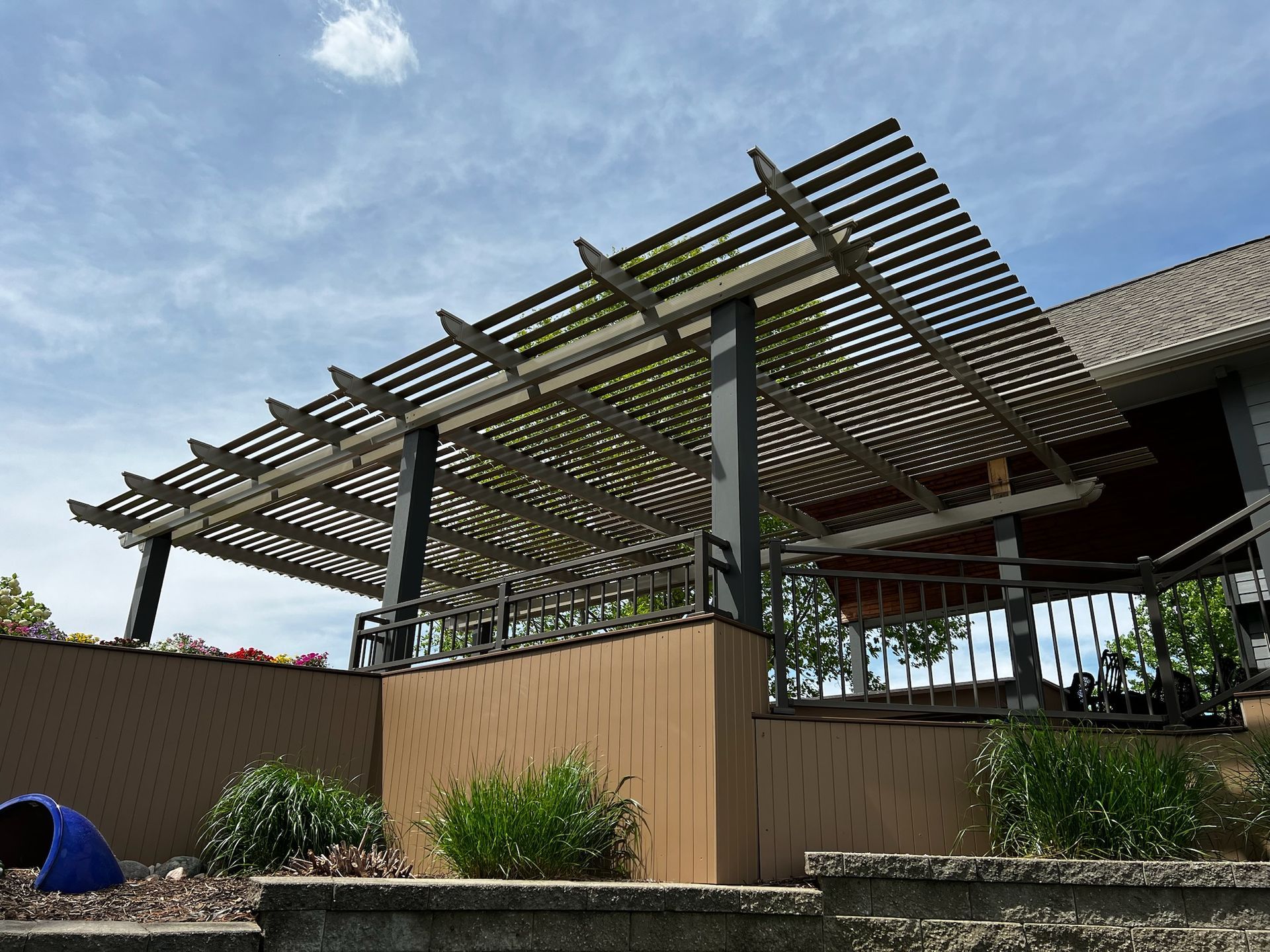 Backyard patio with wooden pergola, slatted shade roof, and raised planter beds under a blue sky