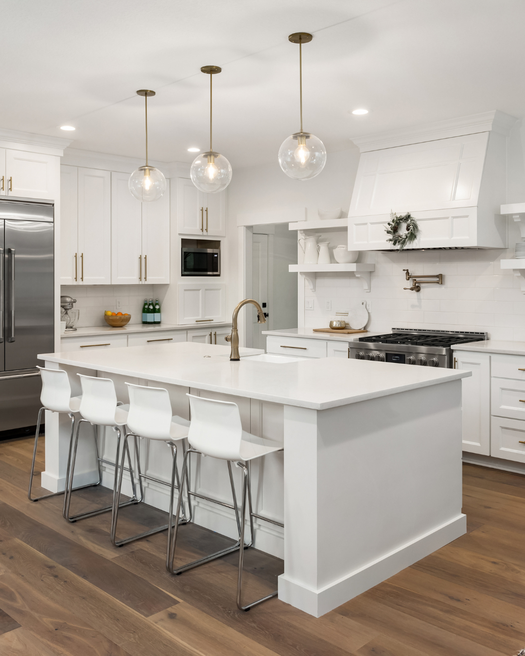 White kitchen with island, pendant lights, and bar stools. Hardwood floor.