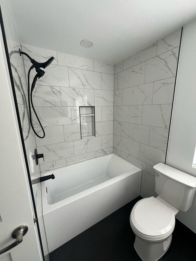 Modern bathroom with white tub, marble-look tile, black fixtures, and dark floor.