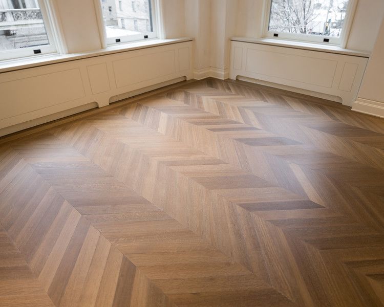 Light wood parquet floor in a chevron pattern, beneath white window frames and trim.
