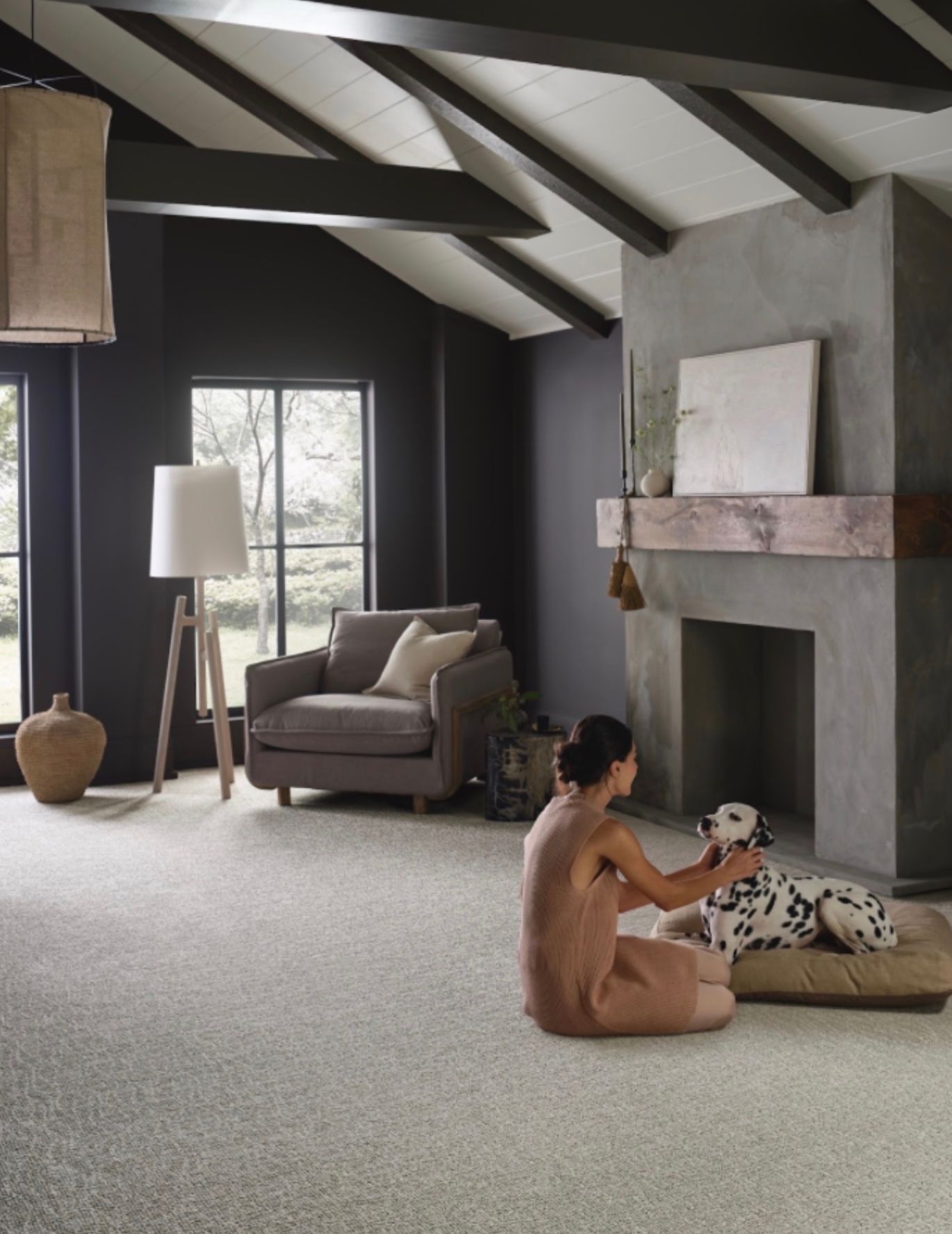 Woman in a neutral dress petting a Dalmatian in a dark, cozy living room with a fireplace.