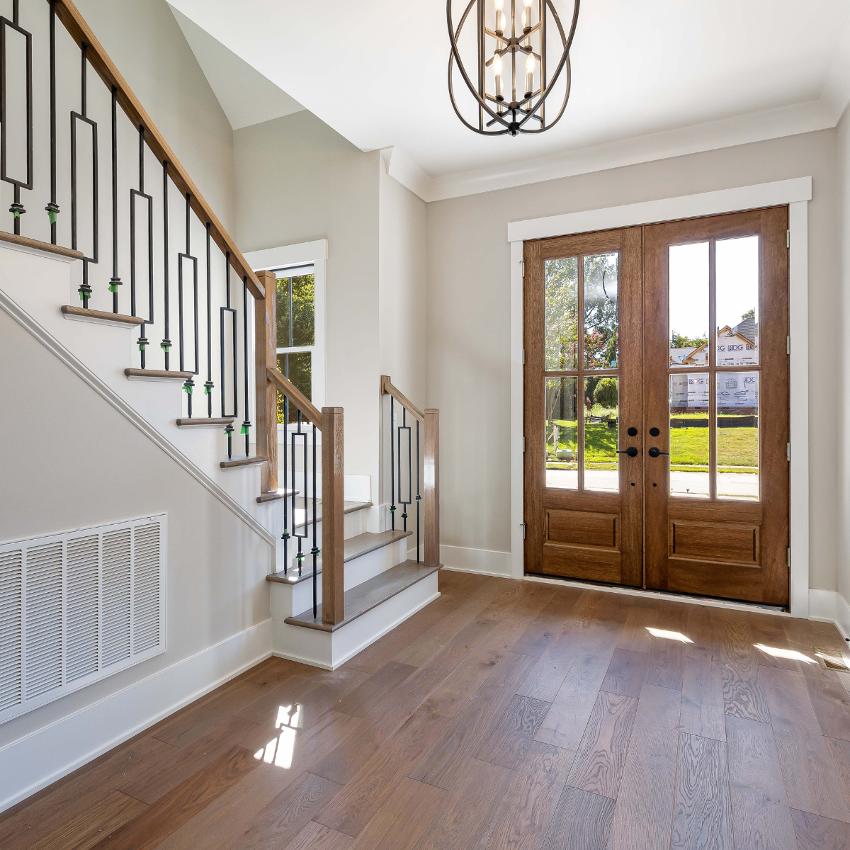 Entryway with wooden double doors and a staircase. Natural light illuminates the hardwood floors.
