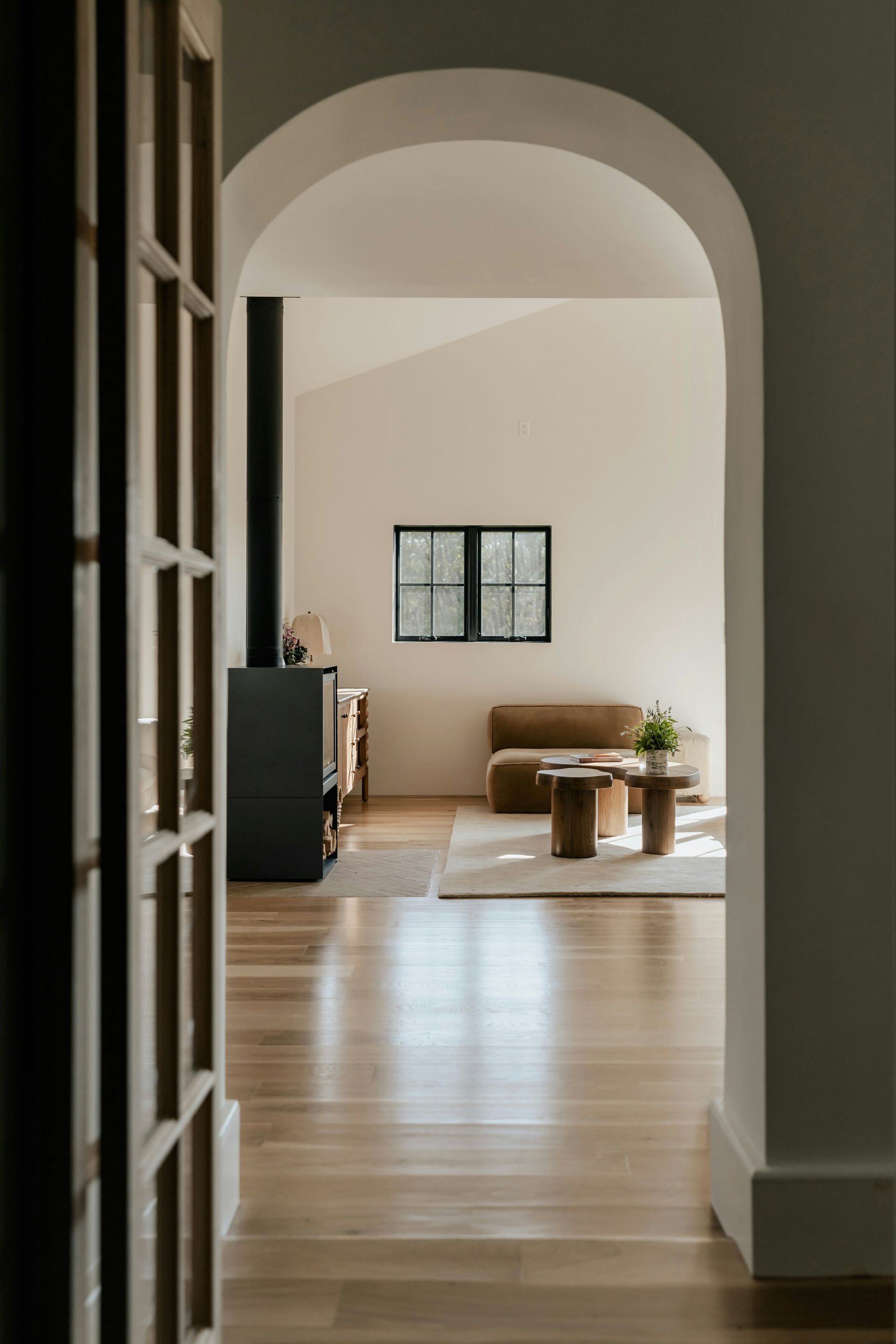 Wooden floor leading to living area with tan sofa, neutral walls, and archway.