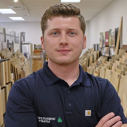 Man in blue shirt stands in a flooring store, arms crossed, smiling.