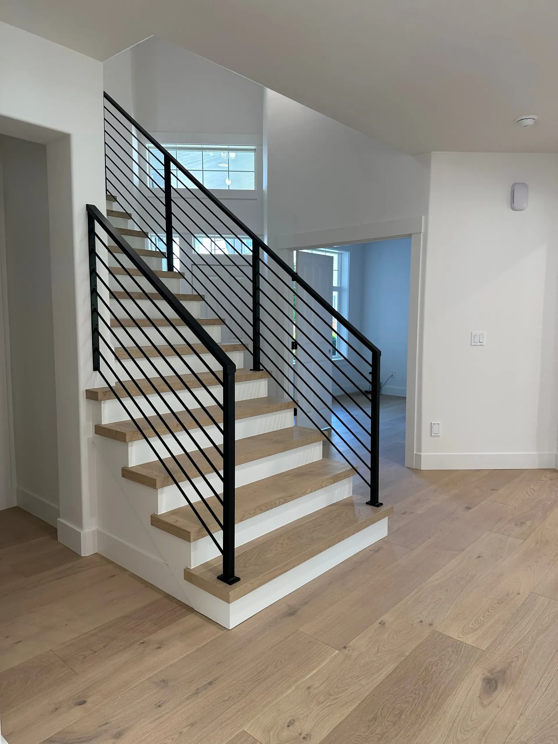 Staircase with black metal railings, white risers, and wooden treads, leading upstairs in a home.