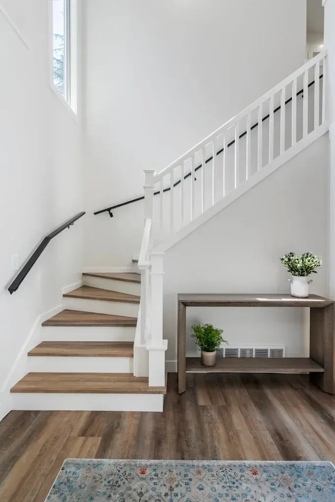 Interior view of a white staircase with wood-toned steps. A gray console table holds plants.