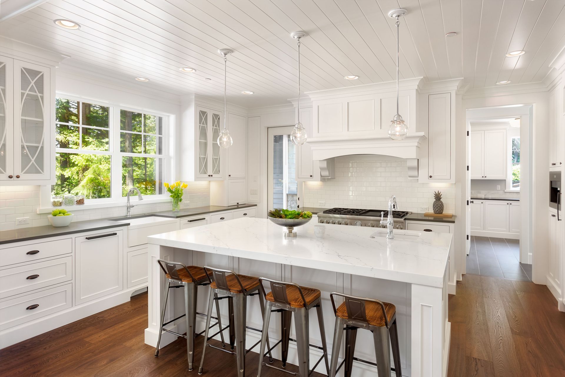 Modern kitchen with white island, wooden stools, and pendant lights.