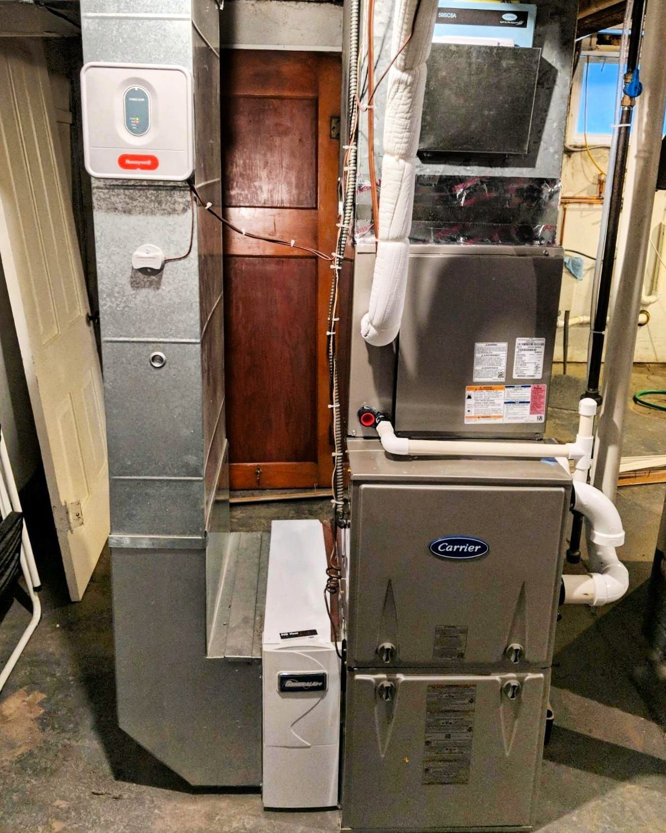 A stainless steel furnace is sitting in a basement next to a door.