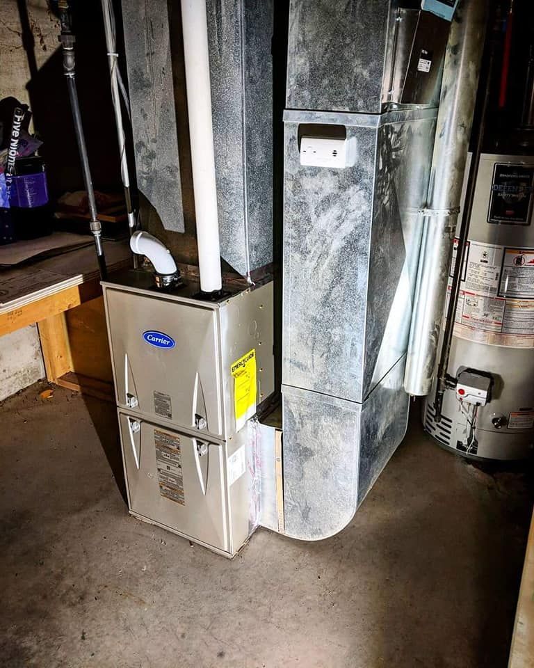 A furnace is sitting next to a water heater in a basement.
