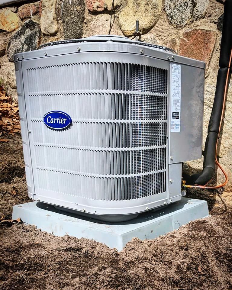 A carrier air conditioner is sitting on top of a pile of dirt next to a stone wall.