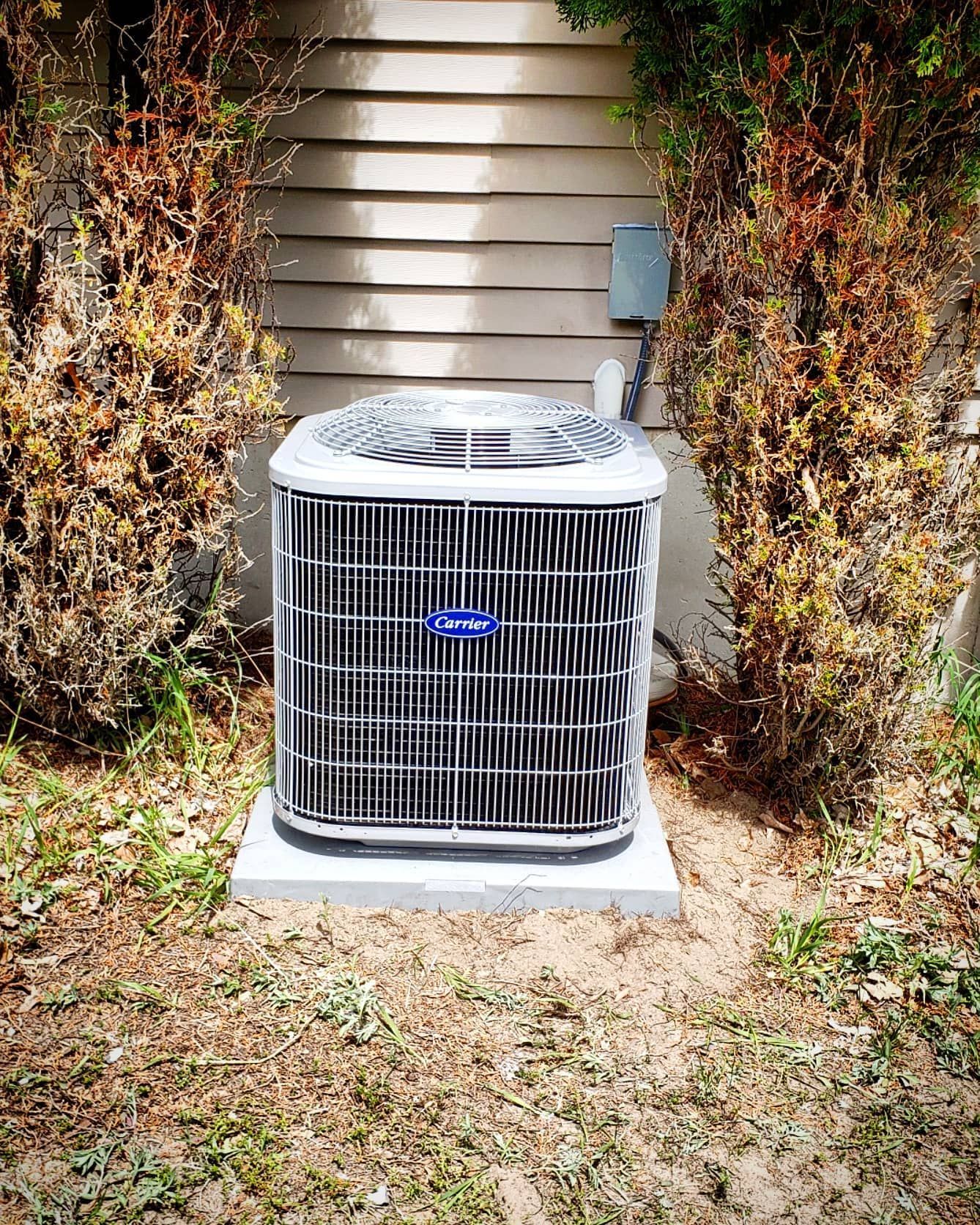 A carrier air conditioner is sitting in the grass in front of a house.